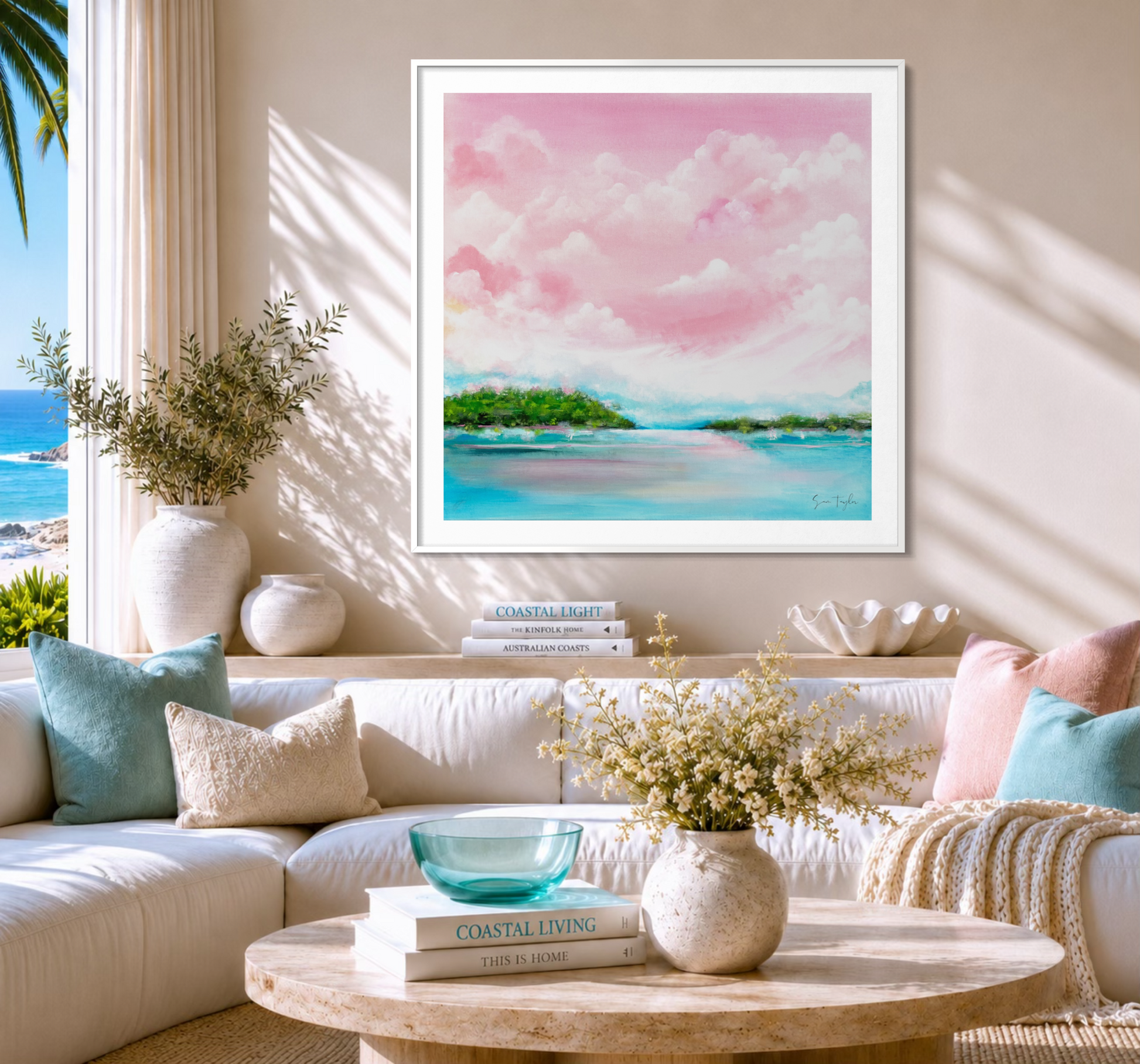 A framed pastel landscape painting of pink clouds and turquoise water is displayed on a beige wall above a white sectional sofa in a bright, modern living room.